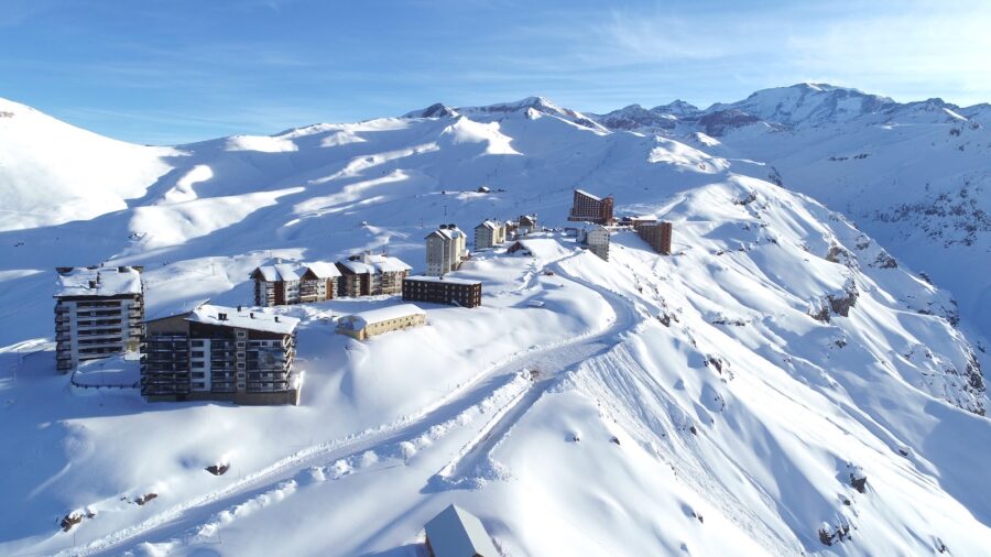 Uma estação de esqui no Chile de alta altitude com prédios modernos aninhados nas encostas cobertas de neve imaculada, sob um céu azul claro, um paraíso para viajar em feriados ou férias de inverno