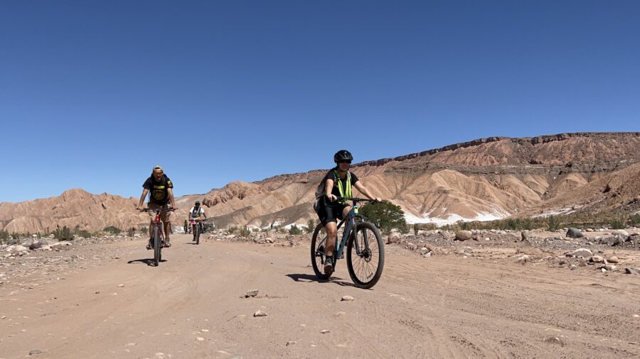 Como economizar no Atacama. | Pessoas andando de bicicleta em uma estrada de terra no deserto com montanhas áridas ao fundo