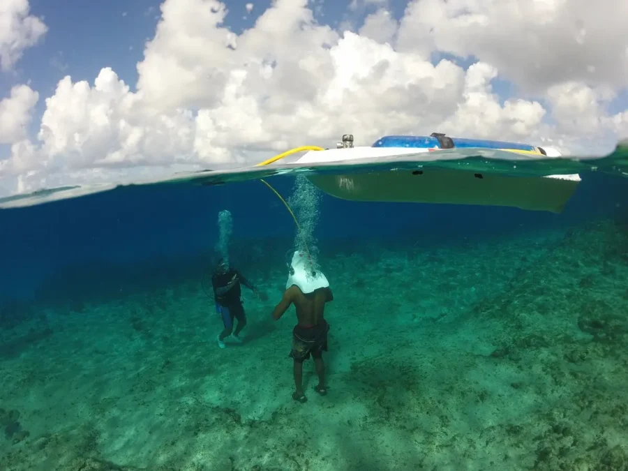 Aquanautas em San Andrés: duas pessoas com capacetes de mergulho cercadas por cardumes de peixes sob a água