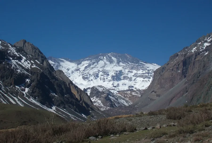 Calcule suas férias: vista de uma imponente montanha coberta de neve e gelo, emoldurada por encostas rochosas escuras sob um céu limpo e azul