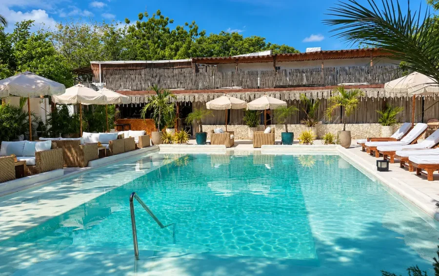 Piscina do Bora Bora Beach Club em Cartagena, cercada por espreguiçadeiras, guarda-sóis, sofás e vegetação tropical, em um ambiente paradisíaco ideal para relaxar durante uma viagem ao Caribe colombiano