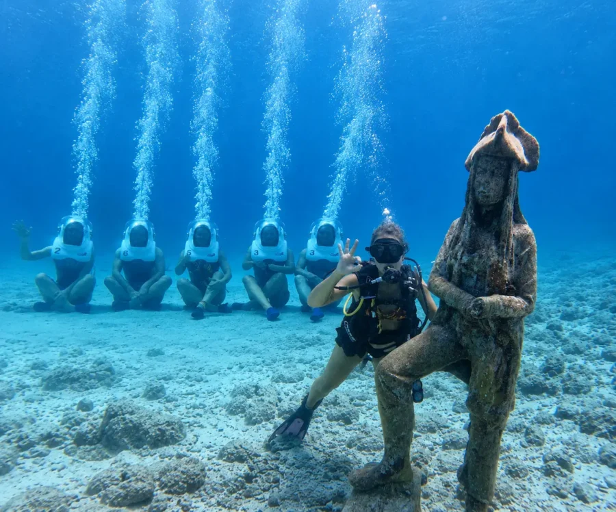 Mergulho com cilindro em San Andrés, com mergulhadores explorando o fundo do mar azul ao lado de uma estátua submersa e turistas usando capacetes de mergulho