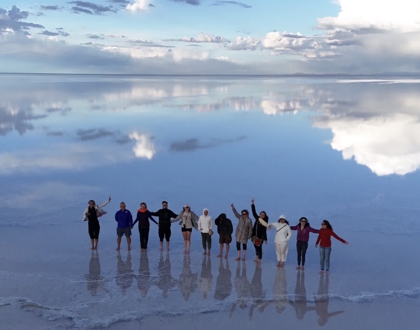 Grupo de viajantes no Salar Espelhado, com seus reflexos no chão coberto de água.