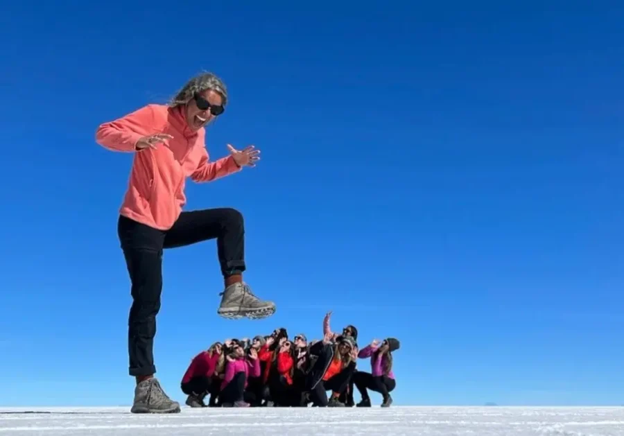 Salar de Uyuni Clássico, Conforto ou VIP: grupo de viajantes no Salar de Uyuni fazendo uma foto com efeito de perspectiva, enquanto uma pessoa aparece em primeiro plano parecendo gigante sobre o grupo, sob um céu azul intenso