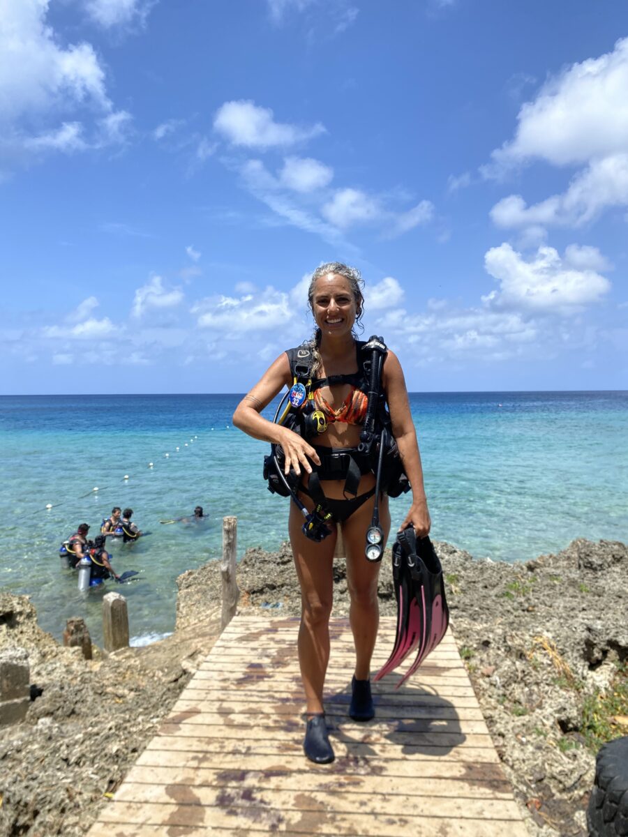 Mergulho com cilindro em San Andrés: turista com equipamento de mergulho e nadadeiras posa em uma plataforma à beira-mar, com águas cristalinas do Caribe ao fundo